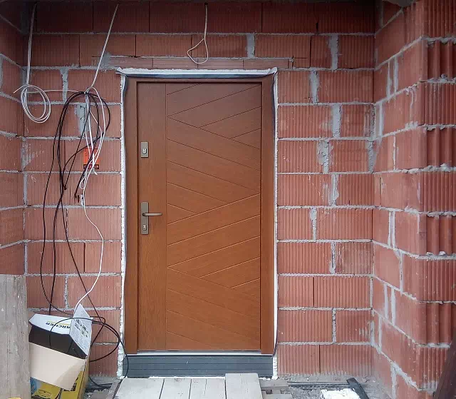 Widok elewacji domu z zamontowanymi drzwiami wzór 430,13 wymalowanymi w kolorze złoty dąb.