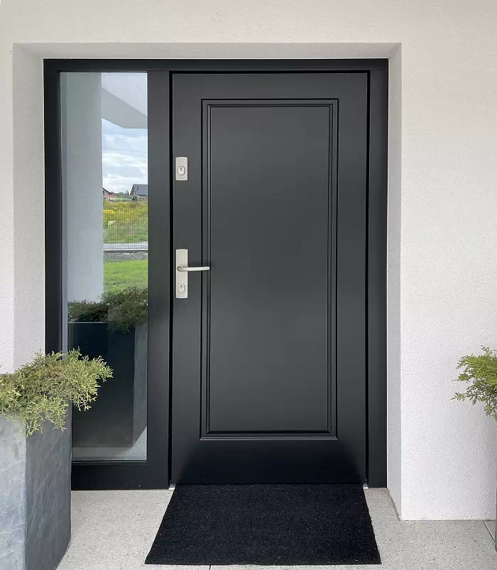 Widok elewacji domu z zamontowanymi drzwiami wzór 535,5 wymalowanymi w kolorze czarne.