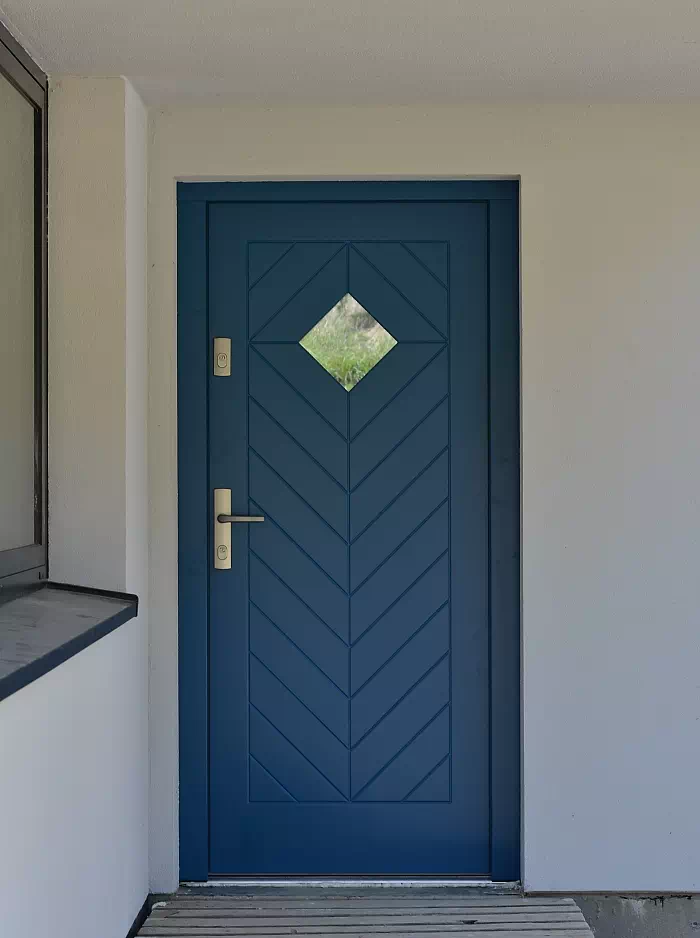 Widok elewacji domu z zamontowanymi drzwiami wzór 543,1C wymalowanymi w kolorze granat.