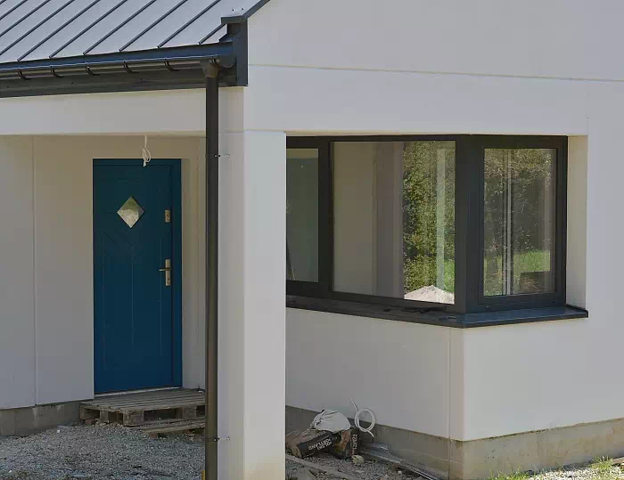 Widok elewacji domu z zamontowanymi drzwiami wzór 543,1C wymalowanymi w kolorze granatowe.