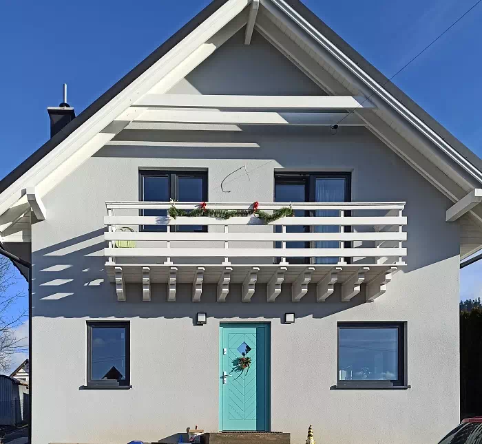 Widok elewacji domu z zamontowanymi drzwiami wzór 543,1C wymalowanymi w kolorze turkusowe.