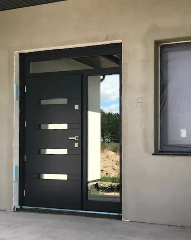 Widok elewacji domu z zamontowanymi drzwiami wzór 422,13 wymalowanymi w kolorze antracyt.