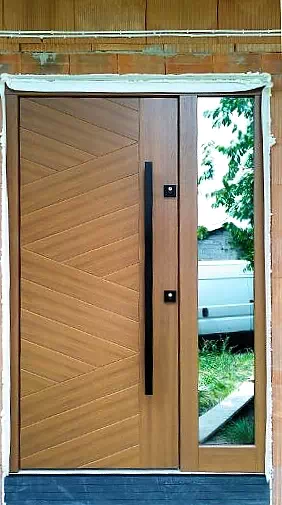 Widok elewacji domu z zamontowanymi drzwiami wzór 430,13 wymalowanymi w kolorze jasny dąb.