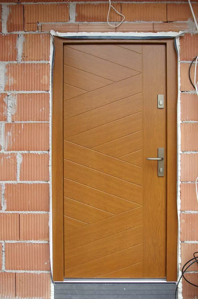 Widok elewacji domu z zamontowanymi drzwiami wzór 430,13 wymalowanymi w kolorze złoty dąb.