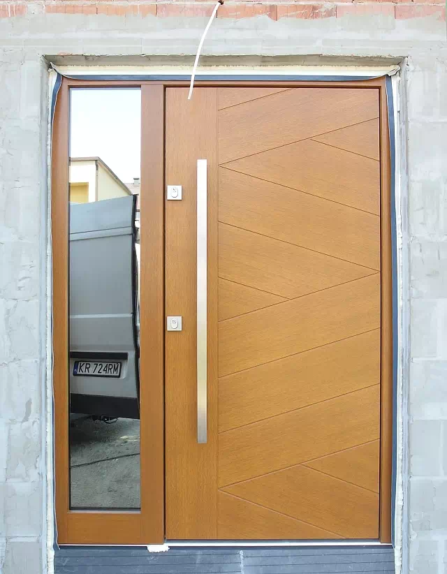 Widok elewacji domu z zamontowanymi drzwiami wzór 430,13B wymalowanymi w kolorze złoty dąb.