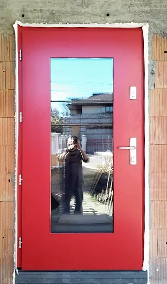 Widok elewacji domu z zamontowanymi drzwiami wzór 499,15z wymalowanymi w kolorze czerwone.