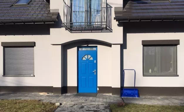 Widok elewacji domu z zamontowanymi drzwiami wzór 506,2 wymalowanymi w kolorze niebieskie.