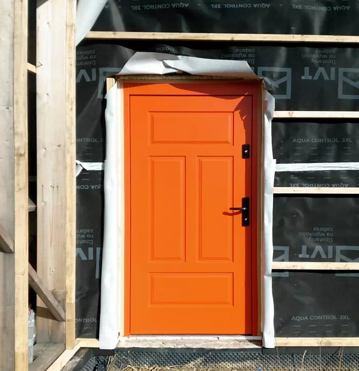 Widok elewacji domu z zamontowanymi drzwiami wzór 533,12 wymalowanymi w kolorze pomarańczowe.