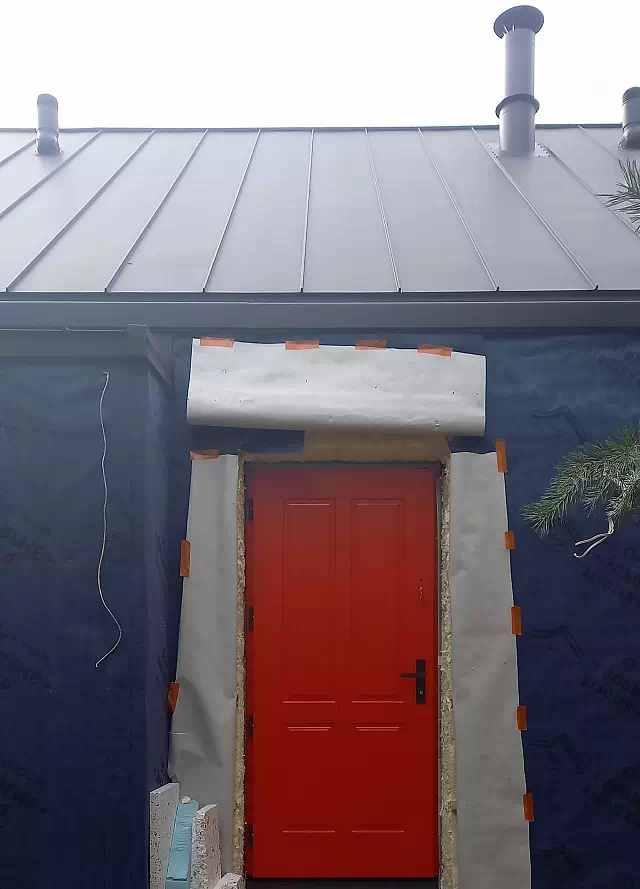 Widok elewacji domu z zamontowanymi drzwiami wzór 534,9 wymalowanymi w kolorze czerwone.