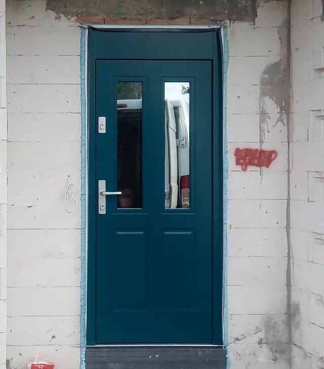 Widok elewacji domu z zamontowanymi drzwiami wzór 534,9B wymalowanymi w kolorze turkusowe.