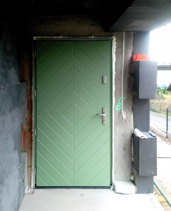 Widok elewacji domu z zamontowanymi drzwiami wzór 542,1 wymalowanymi w kolorze zielone.