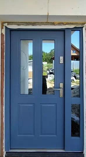 Widok elewacji domu z zamontowanymi drzwiami wzór 534,9B wymalowanymi w kolorze niebieskie.