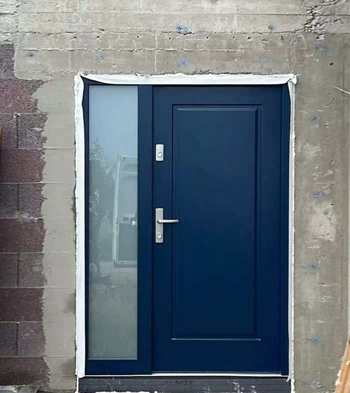 Widok elewacji domu z zamontowanymi drzwiami wzór 535,5 wymalowanymi w kolorze granatowe.