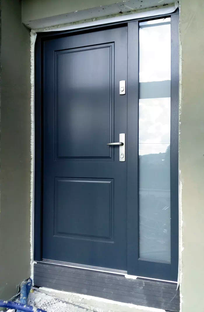 Widok elewacji domu z zamontowanymi drzwiami wzór 535,6 wymalowanymi w kolorze granatowe.