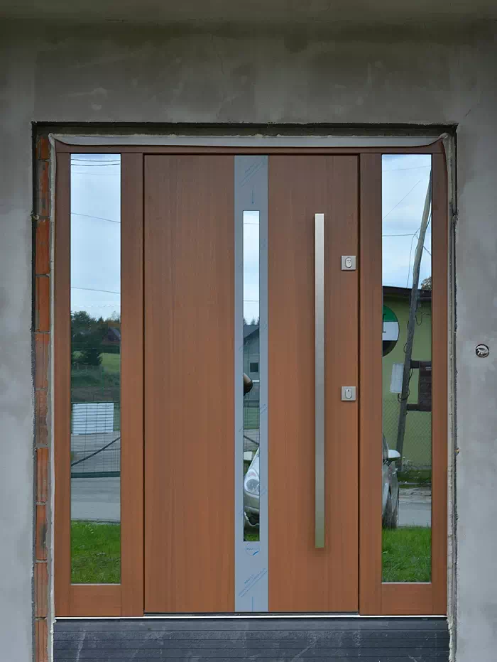 Widok elewacji domu z zamontowanymi drzwiami wzór 454,1 wymalowanymi w kolorze złoty dąb.