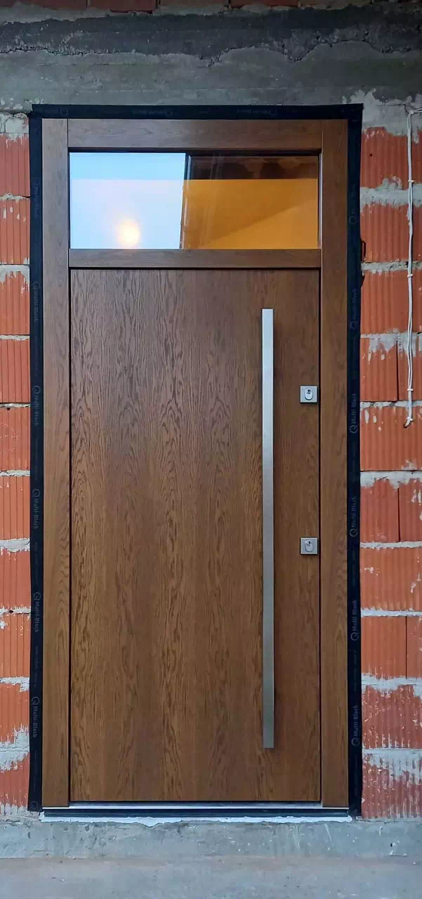 Widok elewacji domu z zamontowanymi drzwiami wzór 500C wymalowanymi w kolorze ciemny dąb.