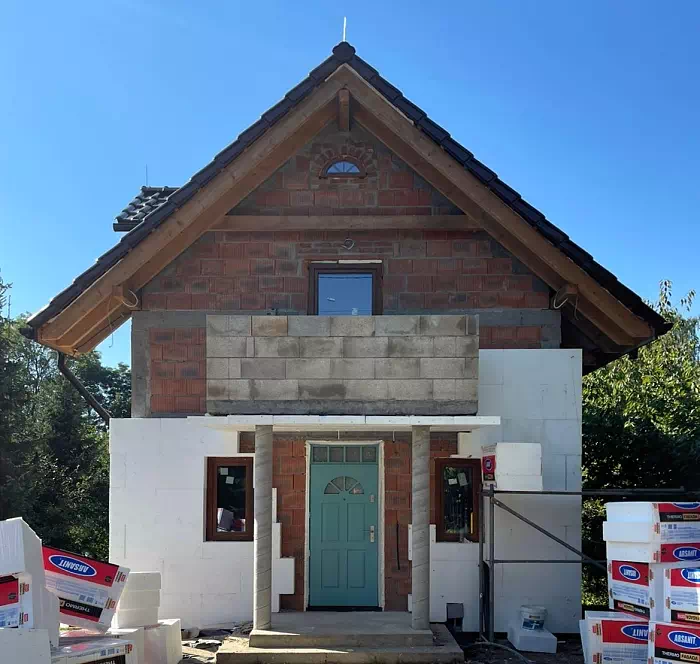 Widok elewacji domu z zamontowanymi drzwiami wzór 506,2 wymalowanymi w kolorze turkusowe.