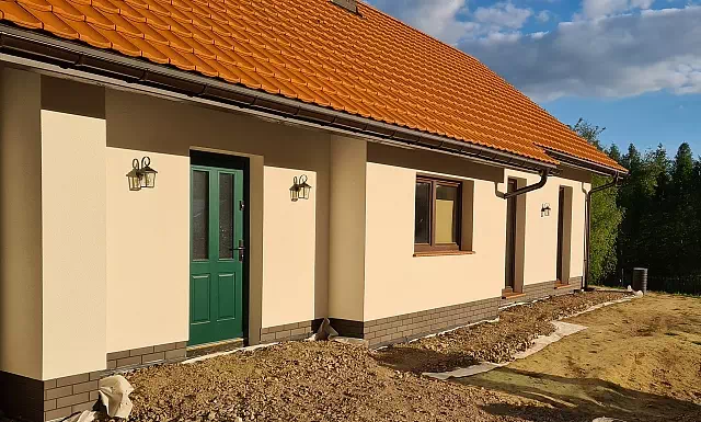 Widok elewacji domu z zamontowanymi drzwiami wzór 534,9B wymalowanymi w kolorze zielone.