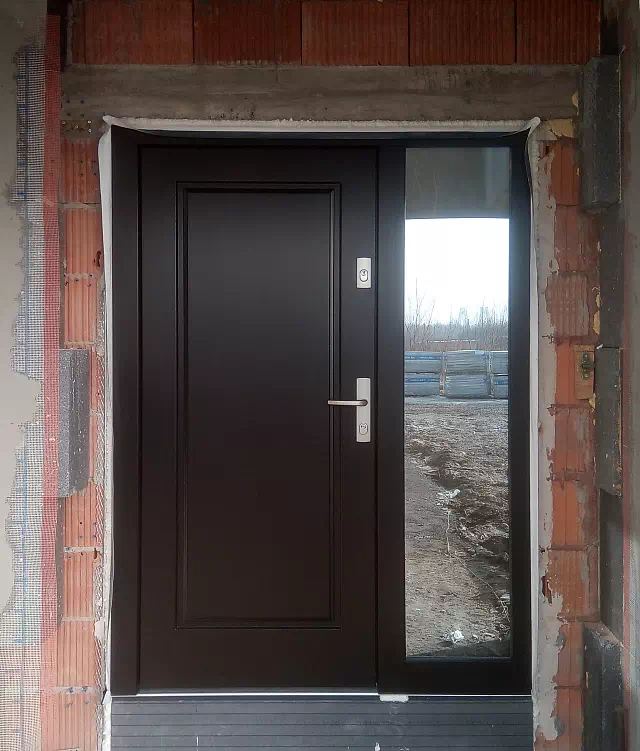 Widok elewacji domu z zamontowanymi drzwiami wzór 535,5 wymalowanymi w kolorze dąb bagienny.