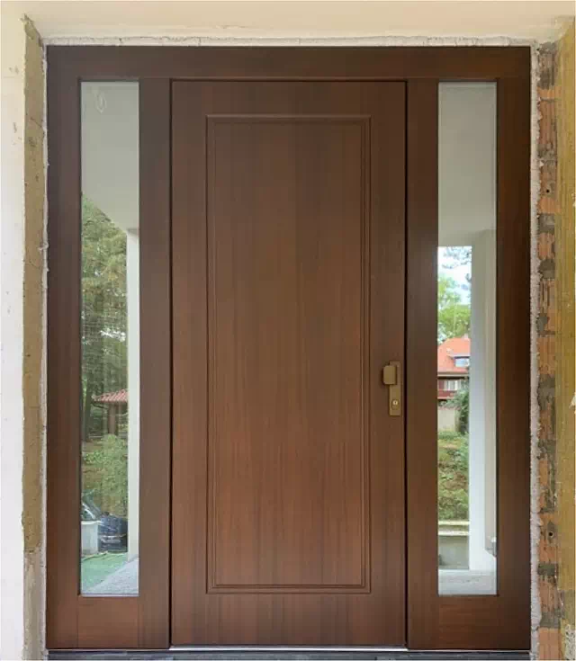 Widok elewacji domu z zamontowanymi drzwiami wzór 535,5 wymalowanymi w kolorze orzech.