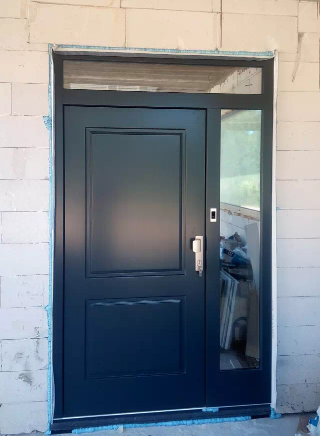 Widok elewacji domu z zamontowanymi drzwiami wzór 535,6 wymalowanymi w kolorze zielone.