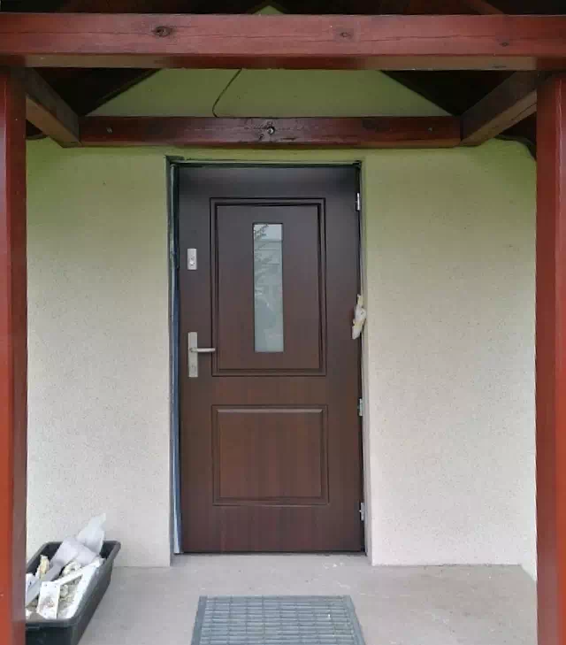 Widok elewacji domu z zamontowanymi drzwiami wzór 535,7 wymalowanymi w kolorze orzech.