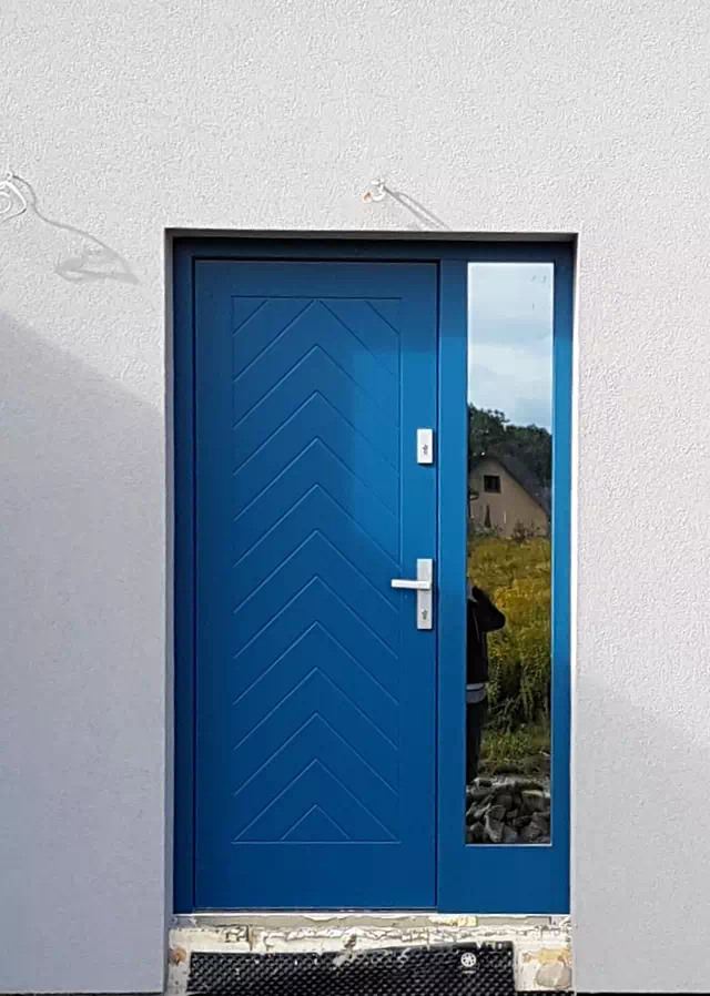 Widok elewacji domu z zamontowanymi drzwiami wzór 543,2 wymalowanymi w kolorze niebieskie.