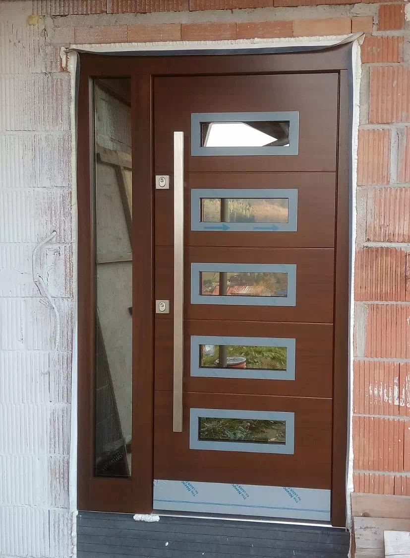 Widok elewacji domu z zamontowanymi drzwiami wzór 898,1 wymalowanymi w kolorze orzech.