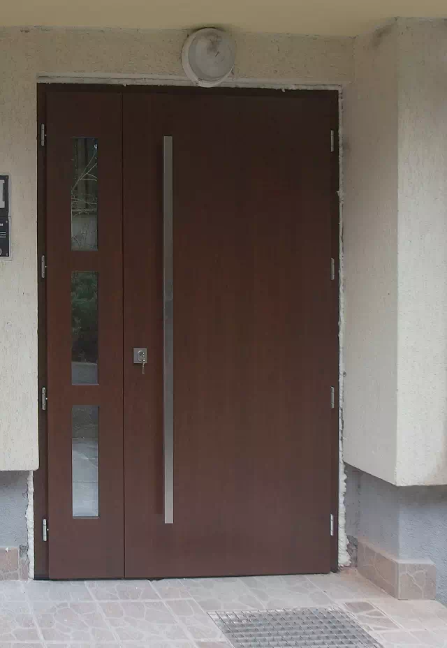 Widok elewacji domu z zamontowanymi drzwiami wzór 500C wymalowanymi w kolorze orzech.