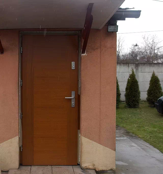 Widok elewacji domu z zamontowanymi drzwiami wzór 500B wymalowanymi w kolorze złoty dąb.