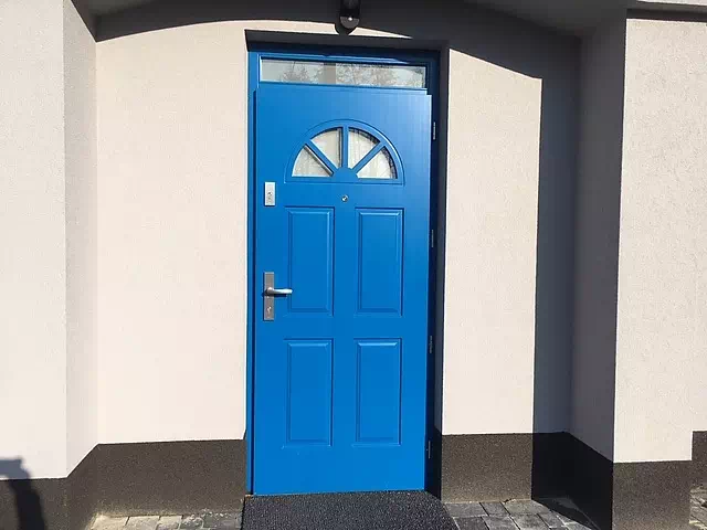 Widok elewacji domu z zamontowanymi drzwiami wzór 506,2 wymalowanymi w kolorze niebieskie.