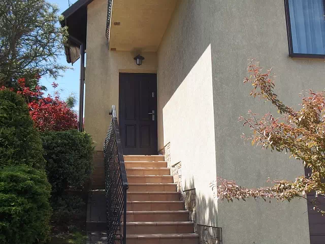 Widok elewacji domu z zamontowanymi drzwiami wzór 534,9 wymalowanymi w kolorze dąb bagienny.