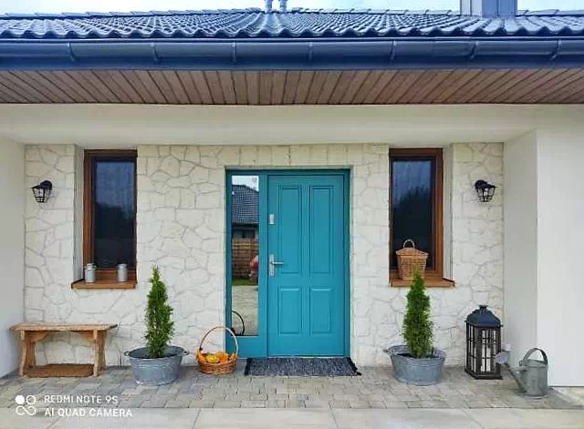 Widok elewacji domu z zamontowanymi drzwiami wzór 534,9 wymalowanymi w kolorze niebieskie.