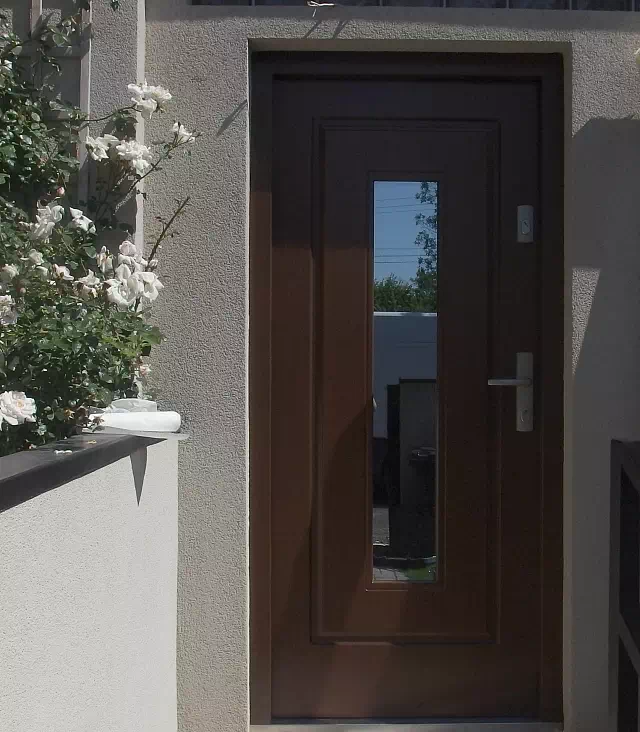 Widok elewacji domu z zamontowanymi drzwiami wzór 572s2 wymalowanymi w kolorze orzech.