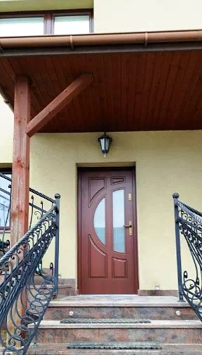 Widok elewacji domu z zamontowanymi drzwiami wzór 599s2 wymalowanymi w kolorze teak.