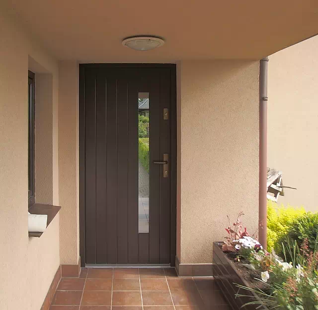 Widok elewacji domu z zamontowanymi drzwiami wzór 689,7s1 wymalowanymi w kolorze czarne.