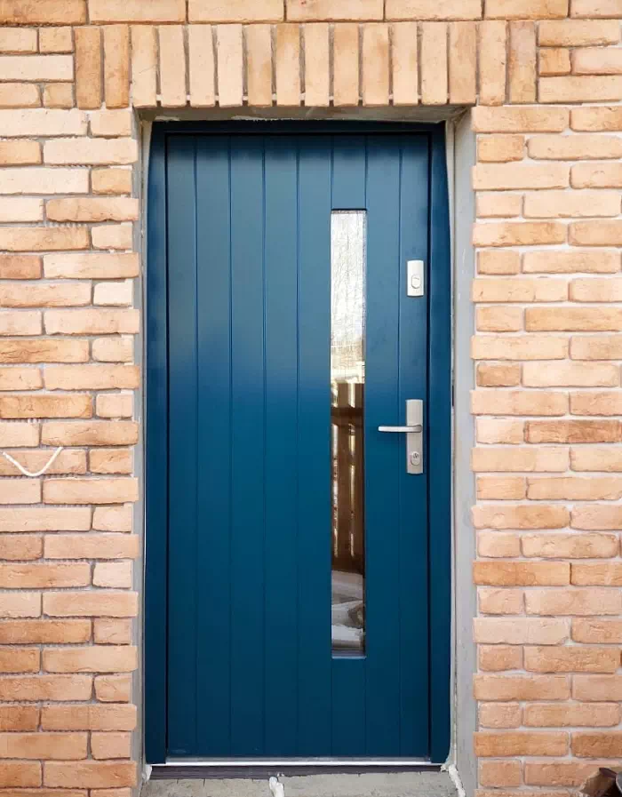 Widok elewacji domu z zamontowanymi drzwiami wzór 689,7s1 wymalowanymi w kolorze niebieskie.