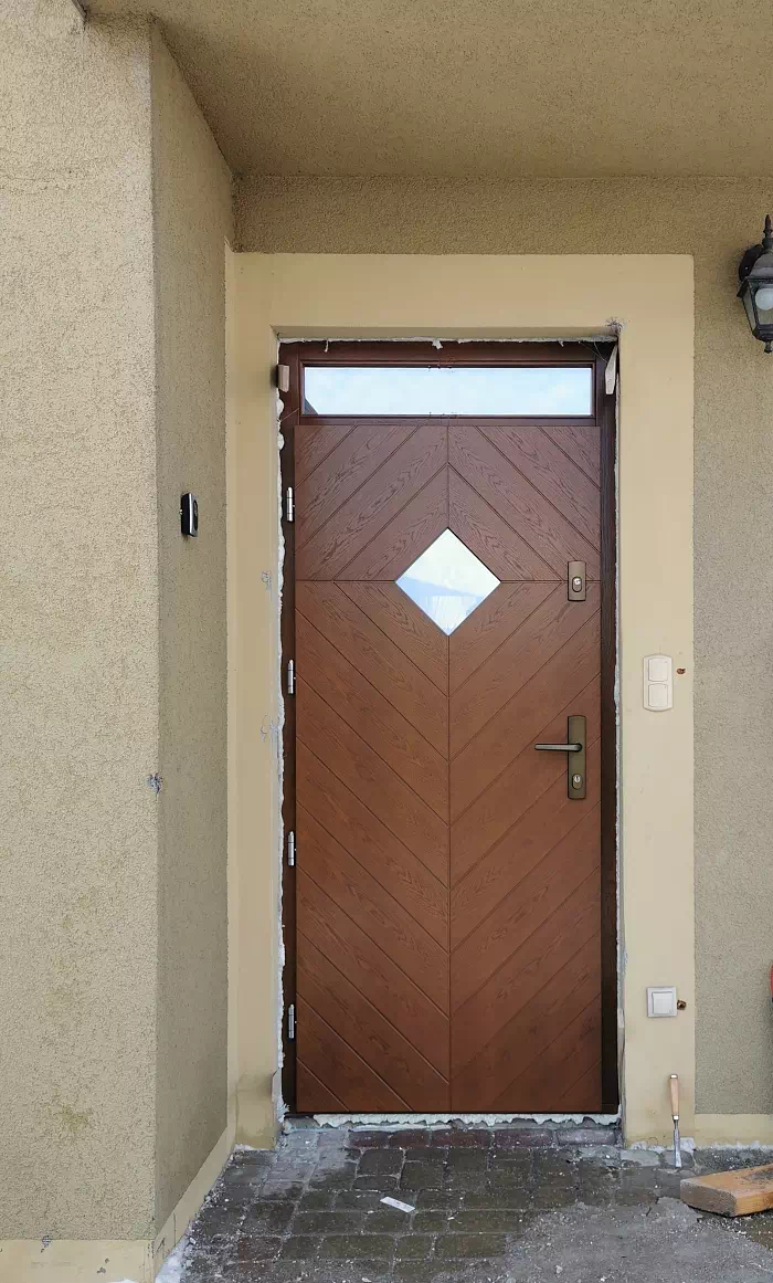 Widok elewacji domu z zamontowanymi drzwiami wzór 543,7 wymalowanymi w kolorze ciemny dąb.
