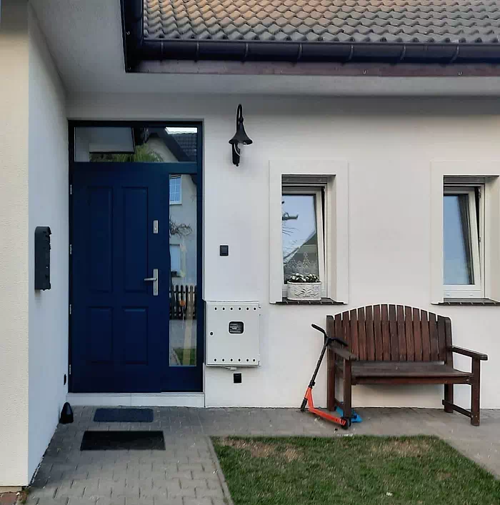 Widok elewacji domu z zamontowanymi drzwiami wzór 534,9 wymalowanymi w kolorze granatowe.