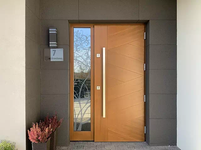 Widok elewacji domu z zamontowanymi drzwiami wzór 430,13b wymalowanymi w kolorze złoty dąb.