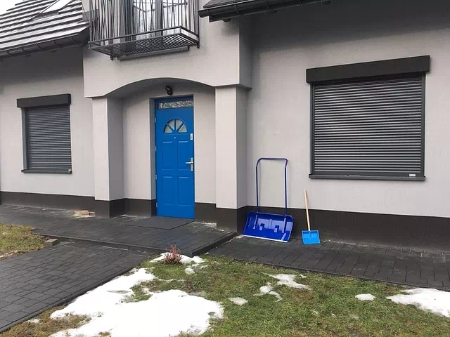 Widok elewacji domu z zamontowanymi drzwiami wzór 506,2 wymalowanymi w kolorze niebieskie.