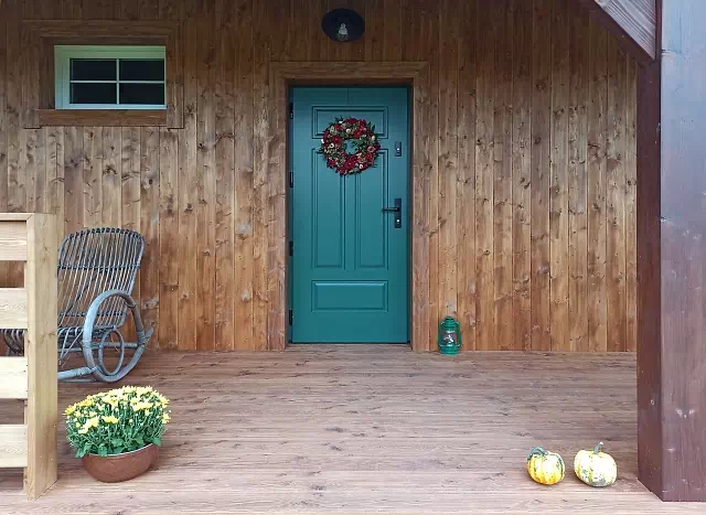 Widok elewacji domu z zamontowanymi drzwiami wzór 533,12 wymalowanymi w kolorze turkusowe.