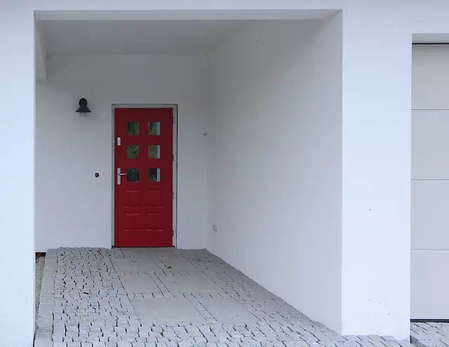 Widok elewacji domu z zamontowanymi drzwiami wzór 574,1 wymalowanymi w kolorze czerwone.